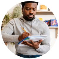 a multi-racial man listing down his expenses on a notebook using a pencil